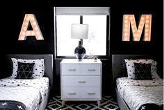 two twin beds in a black and white bedroom with lights on the wall above them