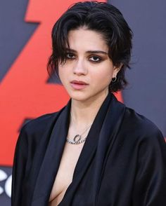 a close up of a person wearing a black suit and necklace with an evil look on her face