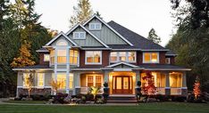 a large house with lots of windows and lights on it's front porch in the evening