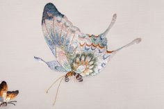 an embroidered butterfly on white fabric with orange, blue and green details in the wings