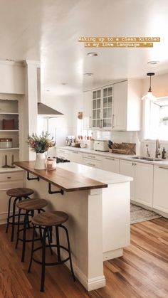 a large kitchen with white cabinets and wooden flooring, along with two stools at the island