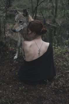 a woman sitting in the woods with a wolf on her back, looking down at her