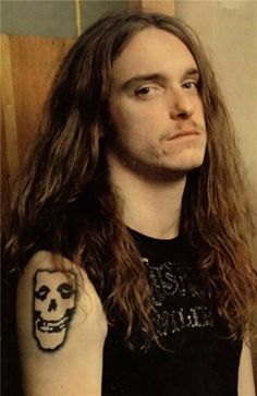 a man with long hair and a skull tattoo on his arm is looking at the camera