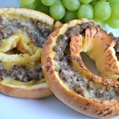 two bagels with meat and cheese are on a plate next to some green grapes