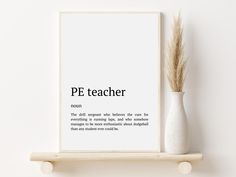 a white vase sitting on top of a wooden shelf next to a framed print that says pe teacher