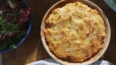 a pie sitting on top of a wooden table next to a bowl of vegetables and a salad