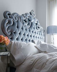 a blue headboard in a bedroom with white sheets and flowers on the side table