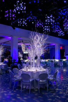 a banquet hall with tables and chairs covered in white tablecloths, lit by blue lights