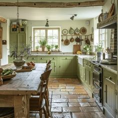 a kitchen with green cabinets and an old fashioned table in the center is surrounded by pots, pans, and other cooking utensils