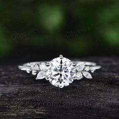 a close up view of a diamond engagement ring on a piece of wood with greenery in the background