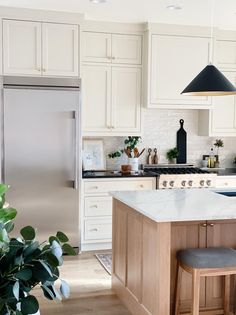 a kitchen with white cabinets and an island in front of a refrigerator freezer next to a potted plant