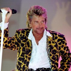 the man is wearing a leopard print jacket and holding a microphone in his right hand