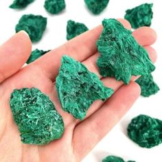 a hand holding some green colored rocks in it's left hand and scattered on the ground