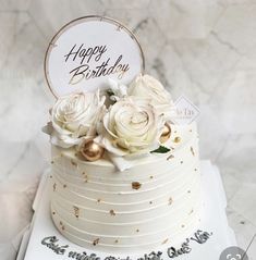 a birthday cake with white flowers and gold confetti on the top is decorated with a happy birthday sign