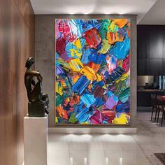 an abstract painting hangs on the wall next to a statue in a room with white tile flooring