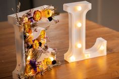 the letters are decorated with flowers and lit up by fairy lights on top of a wooden table