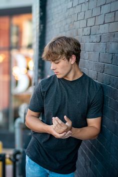 a young man leaning against a brick wall with his hands folded in front of him