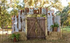 an old wooden gate with hay bales and potted plants on the ground in front of it