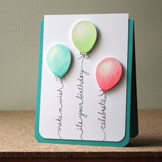 a card with three balloons attached to the back of it, on top of a table