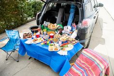 a car trunk full of food and drinks sitting on the side of the road next to a picnic table