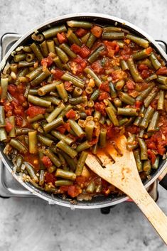 green beans and tomatoes cooking in a pot with a wooden spatula on the side