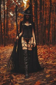 a woman dressed up as a witch holding a broom in the middle of a forest