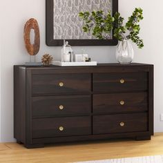 a wooden dresser with two vases and a mirror on the wall above it in a white room