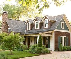 a house with green shutters and brown shingles on the roof, surrounded by greenery