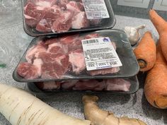 three trays filled with raw meat next to carrots