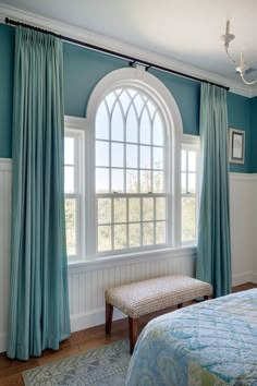 a bedroom with blue walls and curtains on the windowsills, along with a bench