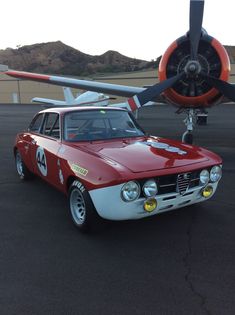 an old race car is parked in front of a plane