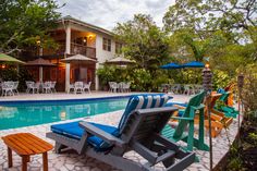 two lawn chairs sitting next to a swimming pool in front of a building with tables and umbrellas