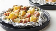 two black plates topped with food covered in aluminum foil on top of a white table