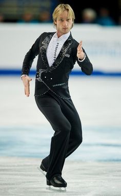 a male figure skating on an ice rink wearing a black suit with silver sequins