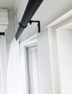 a black pipe is hanging from the side of a white wall next to a window