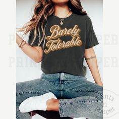 a woman sitting on top of a stool wearing jeans and a t - shirt with the words babey toebake