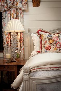 a bed sitting next to a lamp on top of a wooden table in front of a window