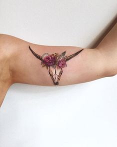 a woman's arm with a cow skull and flowers tattooed on the upper half