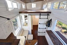 the interior of a tiny house with wood flooring and white walls, looking down into the living room