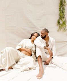 a man and woman sitting on top of a bed next to each other in front of a white backdrop