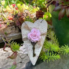 a heart shaped key with a pink flower on it next to succulents