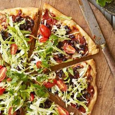 a pizza topped with lots of toppings on top of a wooden cutting board next to a knife and fork