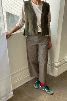 a woman standing in front of a window with her hands on her hips and wearing green shoes