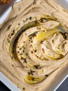 hummus in a square white bowl with a spoon and some bread sticks on the side