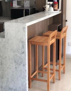 two wooden stools sitting in front of a marble counter top next to a microwave oven