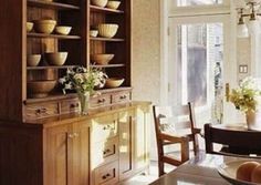 a dining room table and chairs in front of a wooden cabinet with bowls on it