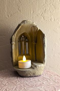 a lit candle sitting on top of a table next to a stone arch shaped like a church