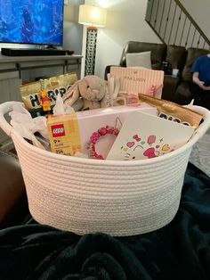 a white basket filled with lots of items on top of a couch next to a tv