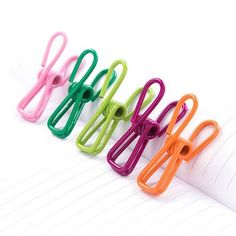 five different colored paper clips sitting on top of an open notebook next to each other