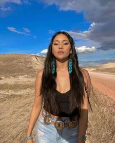 a woman standing in the middle of a dirt road with her eyes closed and wearing turquoise earrings